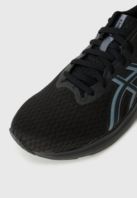 Schwarzer Sportschuh mit einem strukturierten Mesh-Obermaterial, blauen und grauen Akzenten, flachen Schnürsenkeln und einem gerundeten Zehenbereich.