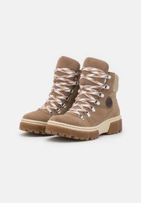 Bottines en daim marron avec des lacets à motifs blancs et marron, détails en métal argenté et semelles en caoutchouc épaisses. Présente un panneau arrière texturé.
