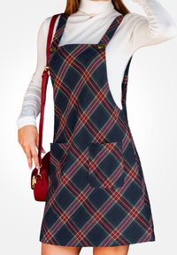 Vestido de tirantes de cuadros en azul marino, rojo y verde. Tiene escote cuadrado, tirantes ajustables y dos bolsillos delanteros. La tela tiene un acabado texturizado.