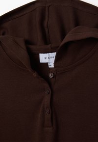 Maglione henley in tessuto a costine marrone con bottoni e texture morbida. Include un colletto e un'etichetta di cura all'interno del collo.