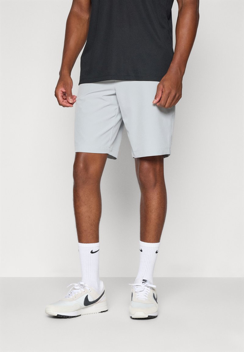 Shorts deportivos grises de tela ligera, combinados con una camiseta negra y calcetines blancos de Nike, completando el look con zapatillas deportivas ligeras.