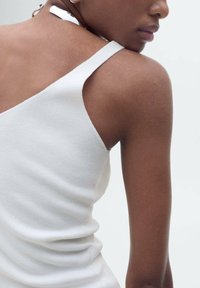 Top bianco a righe con spalline sottili, caratterizzato da una superficie liscia e un design aderente che mette in risalto le spalle e il collo.