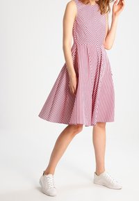 Robe sans manches à rayures rouges et blanches avec un corsage ajusté et une jupe évasée. Associée à des baskets blanches, elle présente une texture de tissu lisse.