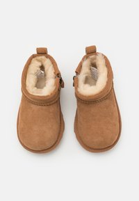 Braune Wildleder-Stiefeletten mit einem kuscheligen cremefarbenen Innenfutter, einer runden Zehenpartie und einem dekorativen Seitenknopf. Weicher Stoff und schlichtes Design.