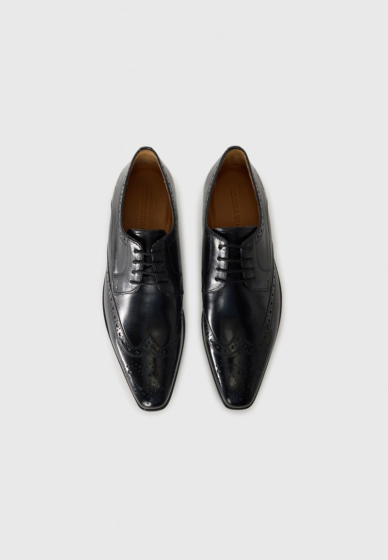 Chaussures habillées en cuir noir avec un design brogue, bouts pointus et perforations détaillées sur les bords. Texture lisse et fermeture à lacets.