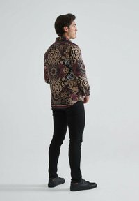 Chemise à boutons avec un motif paisley complexe dans des couleurs sombres, dotée d'un col classique et de manches longues. Associée à un jean skinny noir et des chaussures noires.