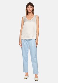 Silk white sleeveless top paired with light blue trousers. Shoes are white with gold accents, featuring a minimalistic design.
