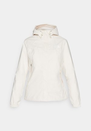 Chaqueta ligera de mujer en color crema, con capucha, puños elásticos, bolsillos frontales y un pequeño logo en el pecho. Textura suave.