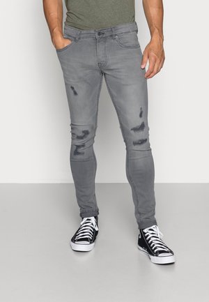 Jeans ajustados grises con detalles desgastados, que cuentan con un diseño de cinco bolsillos y un cierre de botón, combinados con zapatillas de lona en blanco y negro.