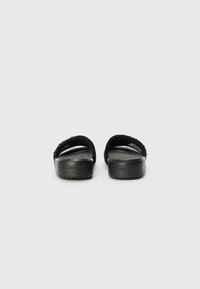Sorte sandaler med en glat overflade, der har et bredt stropdesign og en let hævning i sålen. Branding synlig på hælen.