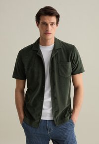 Korte mouwen groene terry shirt met knoopsluiting, notch-kraag en borstzak, gecombineerd met gestreepte blauwe shorts.