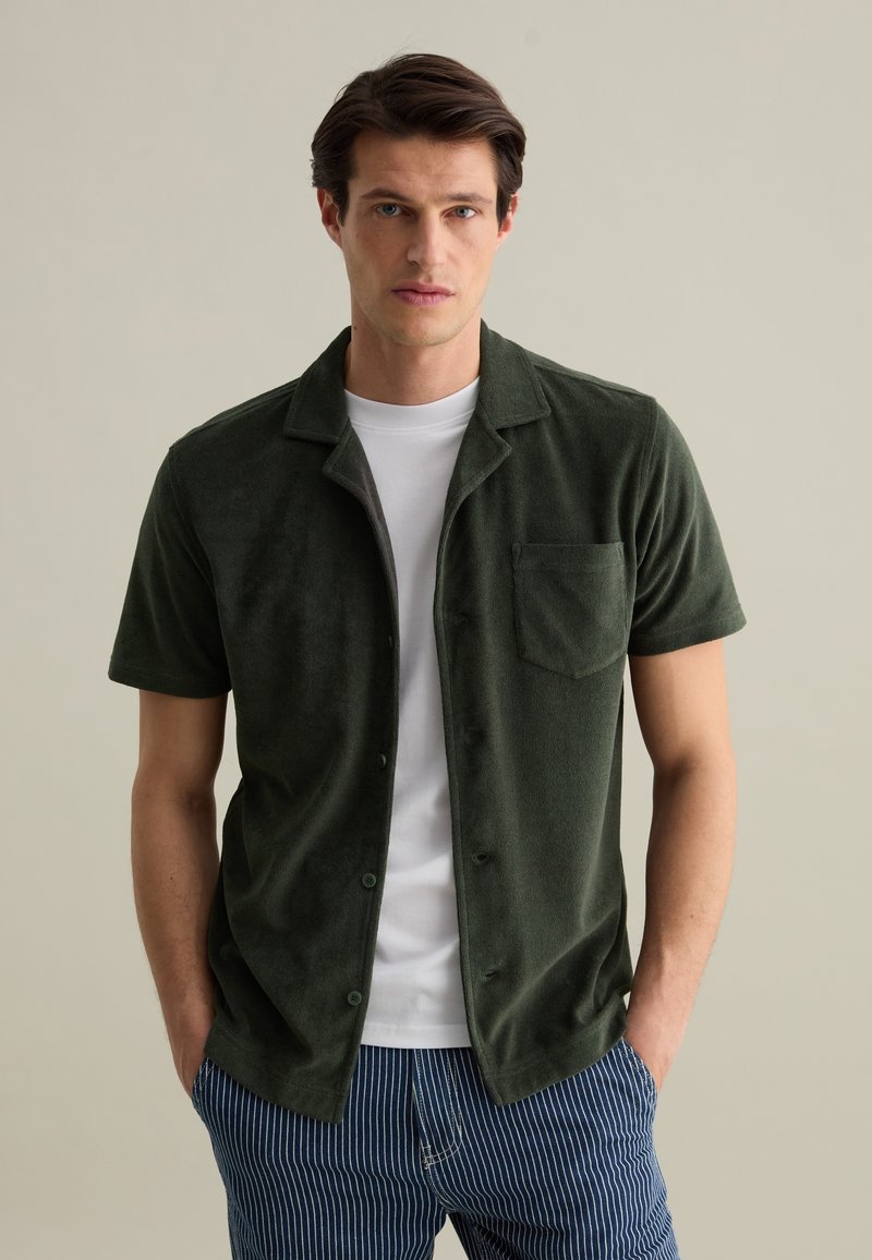 Korte mouwen groene terry shirt met knoopsluiting, notch-kraag en borstzak, gecombineerd met gestreepte blauwe shorts.