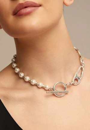 Primer plano del cuello que lleva un collar tipo choker de materiales mixtos, con mitad de cuentas de perlas y mitad de eslabones grandes de cadena plateada, con un cierre de palanca plateado.