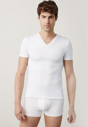 Camiseta blanca de algodón con escote en V y mangas cortas, combinada con bóxer blancos. Textura suave, diseño ajustado y estilo minimalista.