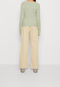 Hellgrüner gerippter Pullover mit körperbetonter Passform und weitem cremefarbenem Hosen. Das Outfit wird von lässigen Sneakers mit einem auffälligen Logo ergänzt.
