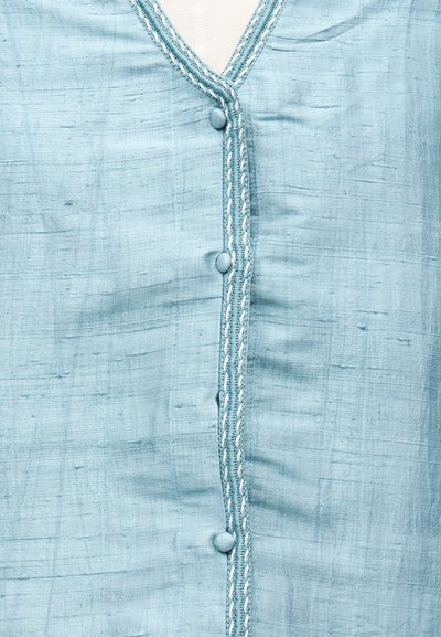 Ανοιχτό μπλε υφαντό ύφασμα με κάθετο κλείσιμο με κουμπιά και διακοσμητική λευκή ραφή κατά μήκος της γραμμής των κουμπιών.