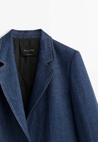 Tummansininen farkkutakki, jossa on sakarat ja näkyvät ompeleet sekä musta sisätagi. Rakenne on jämäkkä ja texture on sileä.