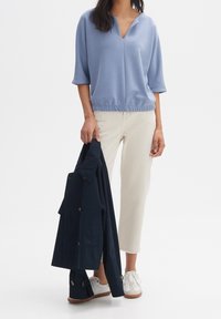 Top in cotone blu chiaro con scollo a V, maniche larghe e orlo arricciato, abbinato a jeans beige e giacca blu navy. Sneakers bianche.