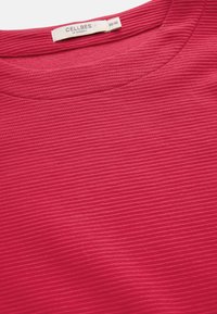 Rød ribbet top med rund halsudskæring. Stoffet har en glat tekstur med diskrete vandrette linjer. Mærkat synlig med mærkenavn og størrelse.