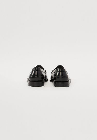 Chaussures en cuir noir avec une texture lisse, bout rond et talon bas. Présentent un design minimaliste et des accents cousus. Vue arrière.