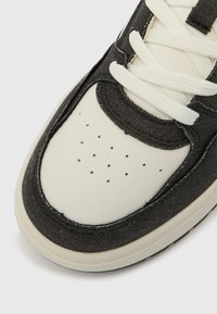 Pantof sport din denim negru și piele crem, cu vârf perforat, șireturi albe și căptușeală moale din material textil, având o formă rotunjită.