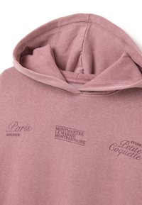 Felpa rosa in tessuto morbido con tasca a marsupio. Presenta stampe testuali: "Parigi" e "Montmartre" in tonalità più scure. Cappuccio dalla vestibilità rilassata.