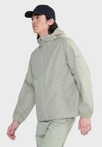 Lichtgroene waterdichte jas met capuchon, ritssluiting, elastische manchetten en Aigle-logo op de linkerschouder. Glad, lichtgewicht stof.