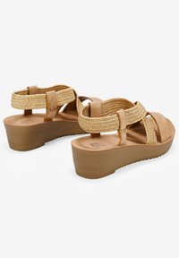 Sandalias de plataforma marrones con correas tejidas beige, que cuentan con una suela texturizada y dos bandas ajustables en el tobillo. Tacón elevado para mayor altura.