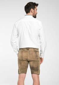 Chemise blanche à manches longues avec des poignets boutonnés, associée à un short en daim marron, doté d'une taille élastique et de poches latérales. Le tissu a une texture lisse.