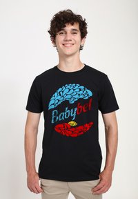 Svart bomulls t-shirt med flerfärgade blommönster och texten 'Babybel' i blått och rött. Korta ärmar, rund halsringning, vanlig passform.