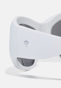 Ochelari de soare albi cu un design îndrăzneț, înfășurător, având lentile închise la culoare și un logo subtil pe lateral. Textură netedă, estetică modernă.