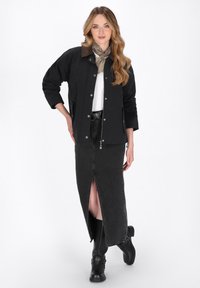 Sort jakke med trykknapper, brun krave, hvid top, sort denimnederdel med høj slids og sorte knæhøje støvler. Lette teksturer hele vejen igennem.