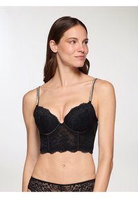 Bralette in pizzo nero con un design strutturato e accorciato. Presenta supporto con ferretto, bordi scallop e spalline decorative in argento.