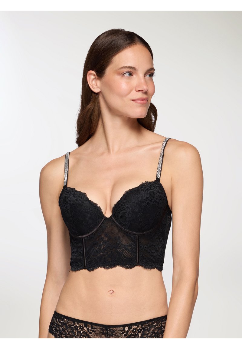 Bralette in pizzo nero con un design strutturato e accorciato. Presenta supporto con ferretto, bordi scallop e spalline decorative in argento.