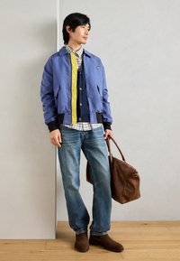 Μπλε bomber μπουφάν με κίτρινη ρίγα, καρό πουκάμισο, σκούρος cardigan, φθαρμένα τζιν, καφέ δερμάτινη τσάντα και καφέ μπότες. Υφή υφάσματος, casual γραμμή.