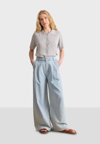 Top de punto de manga corta acanalado en gris claro con cierre de botones, combinado con pantalones de mezclilla anchos en azul claro y sandalias marrones de tiras.