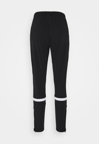 Black athletic pants with an elastic waistband, featuring white stripes around the lower legs and zippers at the cuffs. Smooth fabric texture.