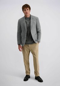 Grijze textuur blazer over een donkergrijze trui, gecombineerd met lichtbeige broeken en zwarte schoenen. Eenvoudige, op maat gemaakte look met zakken.