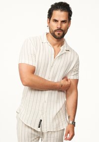 Kurzärmeliges Button-Up-Hemd in hellem Creme mit dünnen vertikalen schwarzen Streifen, strukturiertem Stoff und lässiger Passform. Verfügt über einen Kragen und eine Brusttasche.