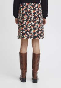 Jupe à motifs floraux sur fond sombre, avec des teintes de rouge, blanc et vert ; accompagnée de bottes en cuir marron jusqu'au genou.