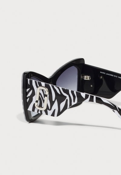 Zwarte cat-eye zonnebril met zebra-print zijkanten, voorzien van een zilveren accent bij de voorsluiting. Gradient lenzen voegen diepte toe aan het ontwerp.