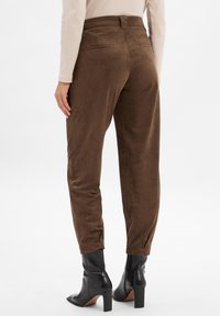 Bruine suede-achtige broeken met een getailleerde pasvorm, twee achterzakken en zijsplitten, gecombineerd met zwarte enkelboots met een blokhak.