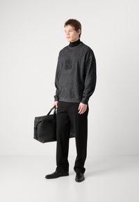 Grå strikket genser med svart "HUGO"-logo, svarte bukser og svart lærveske. Slim-fit design med ribbet tekstur og rund hals.