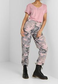 Top corto a maniche corte rosa chiaro con una tasca abbinato a pantaloni cargo mimetici grigi e stivali da combattimento neri con lacci.
