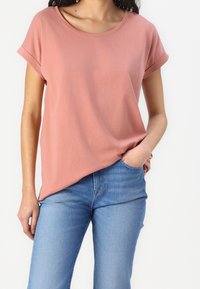 Różowa koszulka z krótkim rękawem, okrągłym dekoltem, luźnym krojem i miękką teksturą, w zestawieniu z niebieskimi dżinsami. Casualowy i prosty design.