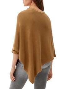Poncho lavorato a maglia marrone con un motivo texture, scollatura ampia e orlo irregolare, che si adagia sulle spalle e abbinato a jeans grigi.