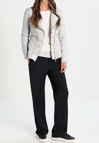 Chaqueta acolchada gris claro con un diseño entallado, combinada con una camiseta blanca y pantalones de pierna ancha azul oscuro. Zapatillas negras completan el conjunto.