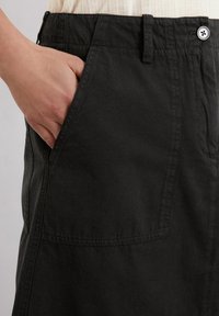 Zwarte katoenen broek met een zijzak, voorzien van een knoopsluiting en een relaxte pasvorm. De stof heeft een gladde, matte textuur.