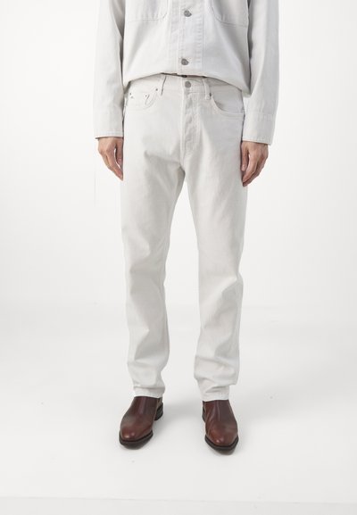 Jean en denim gris clair à coupe droite, avec poches avant, braguette à boutons et détails de couture subtils. Associé à des bottes marron.