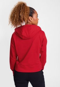 Roter Hoodie mit Kordelzugkapuze, gerippten Bündchen und Saum, der eine glatte Baumwollmischung aufweist. Sieht eng an der Rückseite einer Person aus.